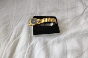 Gold watch and black notebook on a white textile