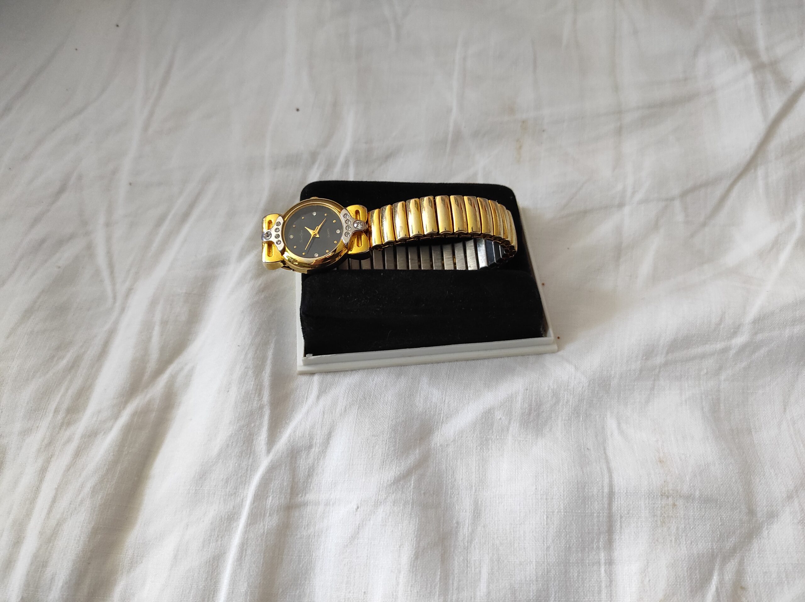 Gold watch and black notebook on a white textile
